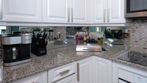 Uma cozinha moderna com armários brancos, bancada de granito, cafeteira Keurig e diversos utensílios de cozinha.