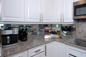 A modern kitchen with white cabinets, a granite countertop, a Keurig coffee maker, and various kitchen utensils.