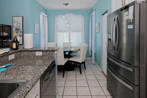 A kitchen with a granite countertop, a stainless steel refrigerator, and a dining area with a table and chairs.
