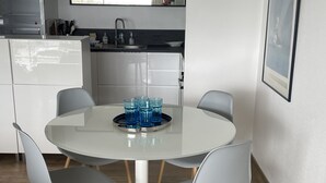 Een moderne keuken met witte kasten, een roestvrijstalen spoelbak en een eethoek met een ronde tafel en vier grijze stoelen.