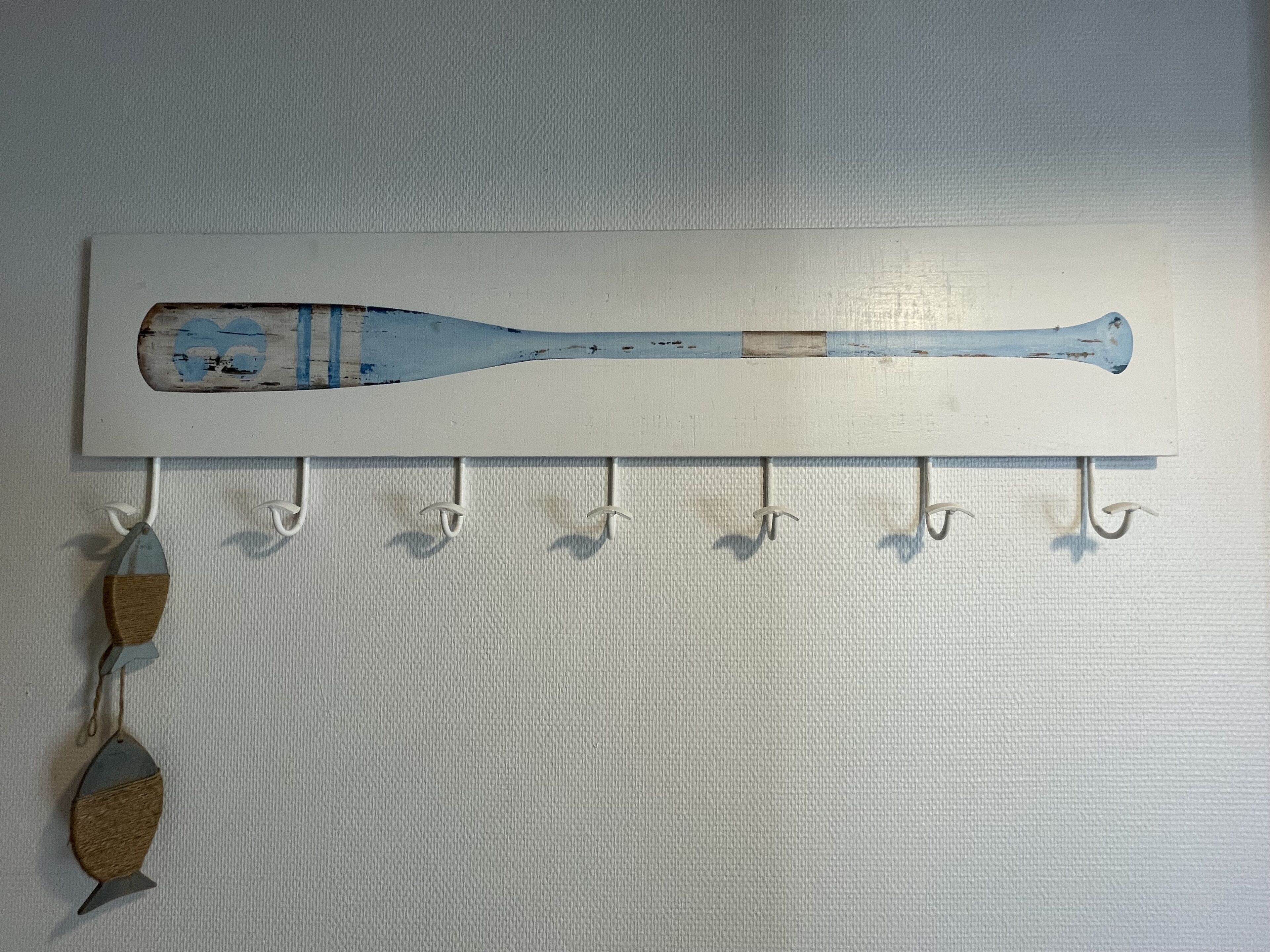 Een houten knuppel hangt aan een witte muur, met haken onder.