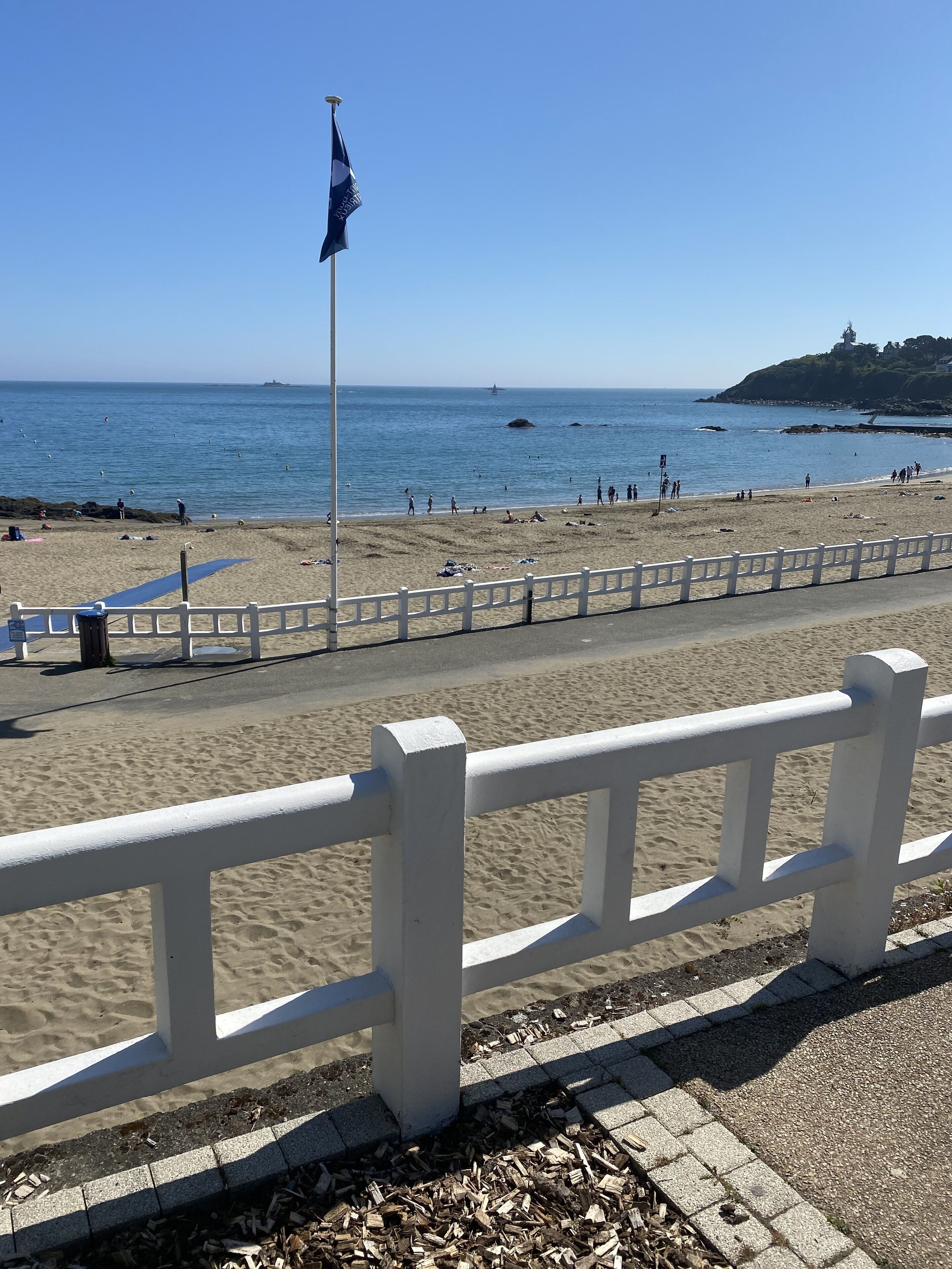 A beach with a white fence, a flag, and a clear blue sky.