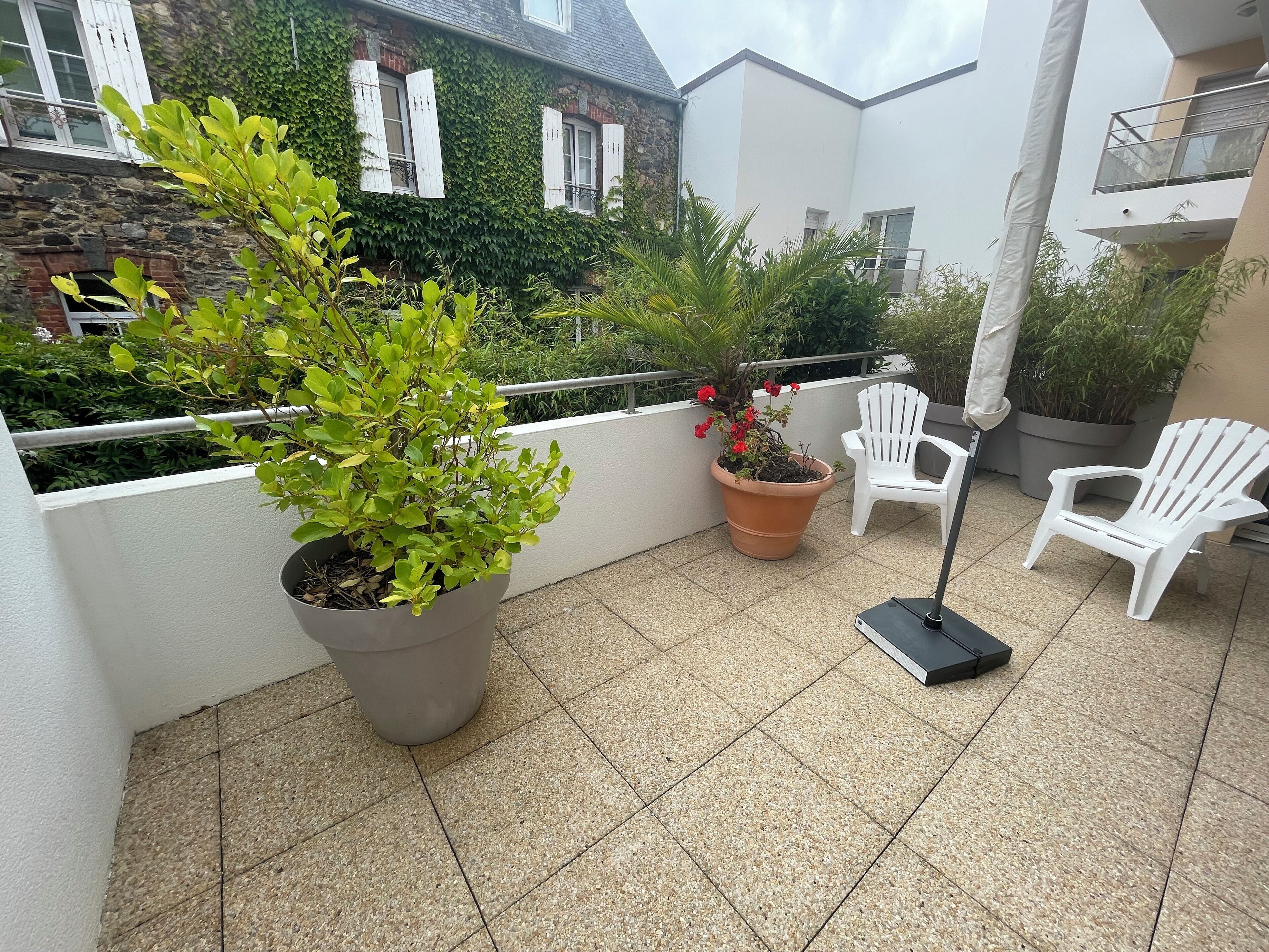 A balcony with potted plants, white chairs, and a tiled floor.