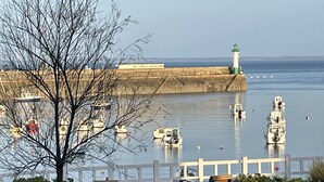 Een promenade aan het water met een houten bankje, een witte hek en een vuurtoren op de achtergrond.