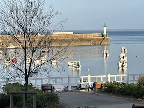 Eine Uferpromenade mit einer Holzbank, einem weißen Zaun und einem Leuchtturm im Hintergrund.