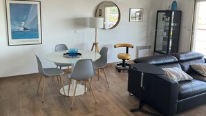 Een moderne woonkamer met een ronde eettafel, grijze stoelen, een zwarte leren bank en een grote spiegel.