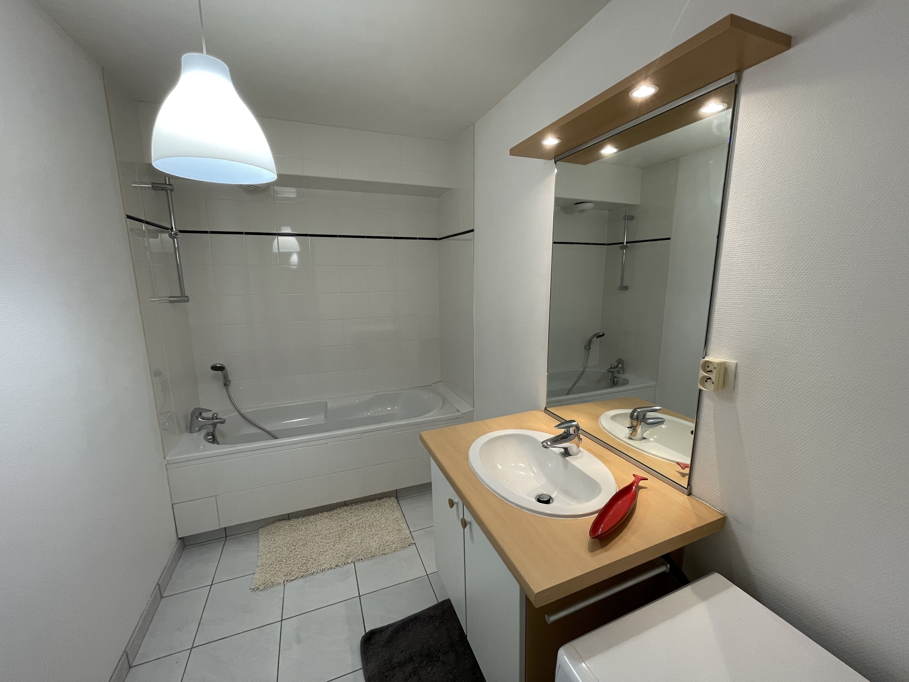 A modern bathroom with a bathtub, two sinks, a mirror, and a light fixture.