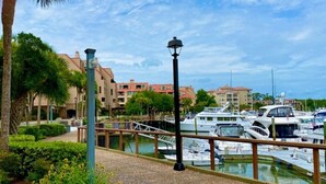 A marina with boats docked, a pedestrian walkway, and buildings in the background. - Lovely Villa Just Steps From The Harbour (Hilton Head Island)