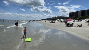 A beach scene with people, umbrellas, and a building in the background. - Lovely Villa Just Steps From The Harbour (Hilton Head Island)