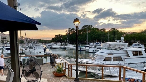 A marina with multiple boats docked, a street lamp, and a person walking. - Lovely Villa Just Steps From The Harbour (Hilton Head Island)