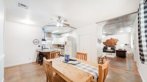 Een ruime keuken met witte kasten, een eethoek met een houten tafel en stoelen, en een zithoek met een bank en salontafel.