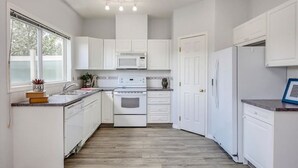 A modern kitchen with white cabinets, a microwave, an oven, and a refrigerator. - Awesome Summer or Stampede Rental (Calgary)