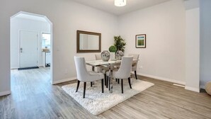 A dining area with a white table, four chairs, a vase, and a mirror on the wall. - Awesome Summer or Stampede Rental (Calgary)