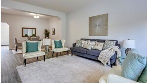 A modern living room with a grey sofa, two white armchairs, a coffee table, and a large abstract artwork on the wall. - Awesome Summer or Stampede Rental (Calgary)
