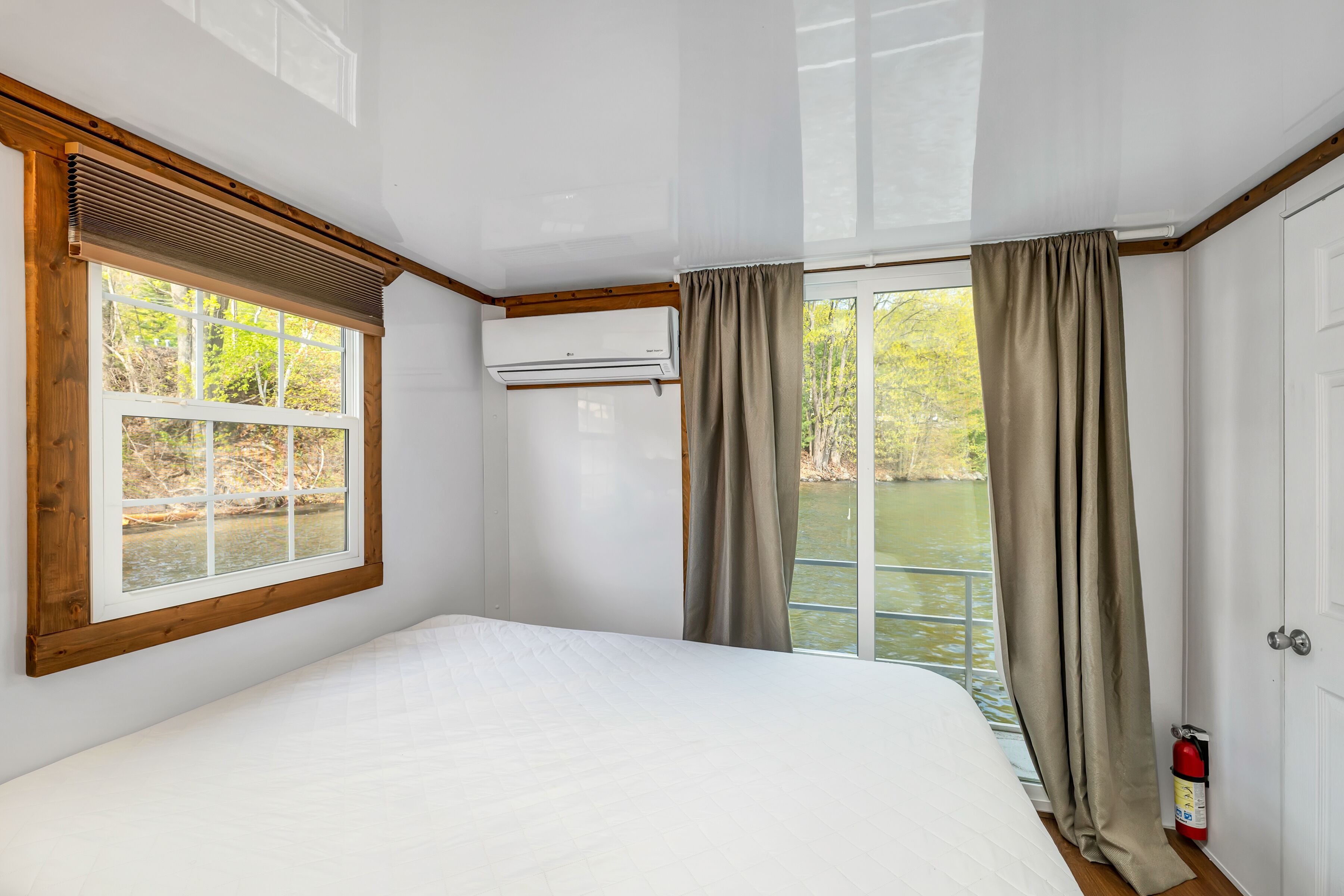 Ein Schlafzimmer mit einem großen Bett, einem Fenster mit Flussblick und einem an der Wand befestigten Feuerlöscher.