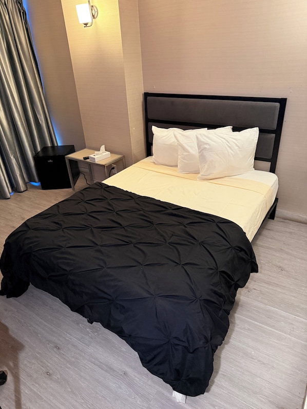 A hotel room with a bed, a bedside table, a lamp, and a black speaker.