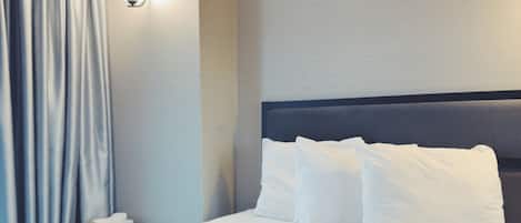 A hotel room with a neatly made bed, a bedside table with a lamp, and a window with curtains.