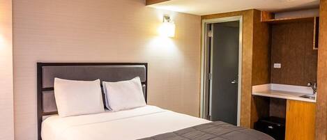 Habitación de hotel con cama, armario empotrado y baño pequeño con lavabo.