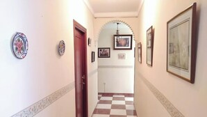 Un couloir avec un sol à carreaux, des tableaux encadrés accrochés aux murs et une porte au fond.