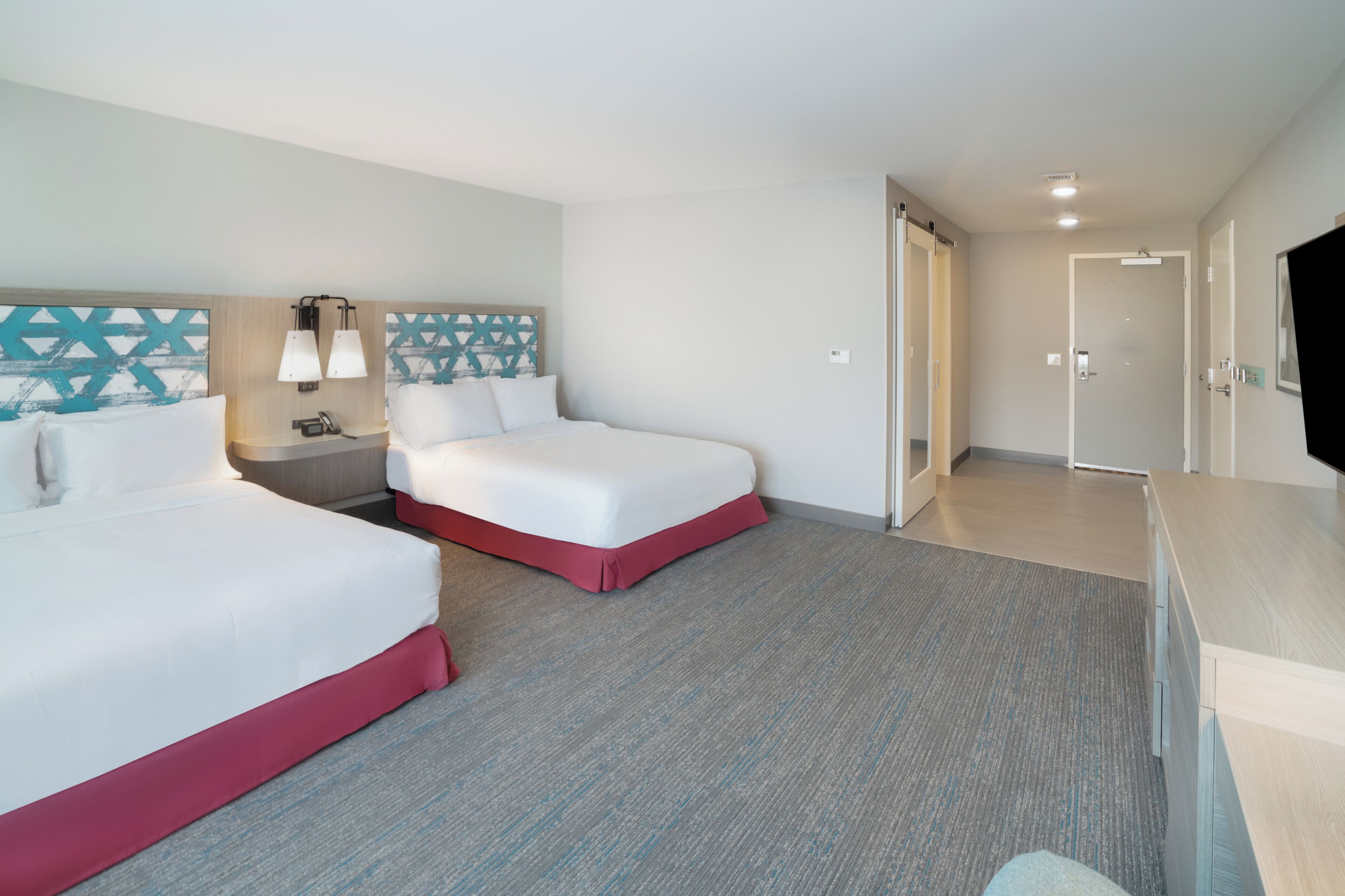 Habitación de hotel con dos camas, un escritorio, un televisor y la puerta del baño.