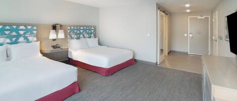 Habitación de hotel con dos camas, un escritorio, un televisor y la puerta del baño.