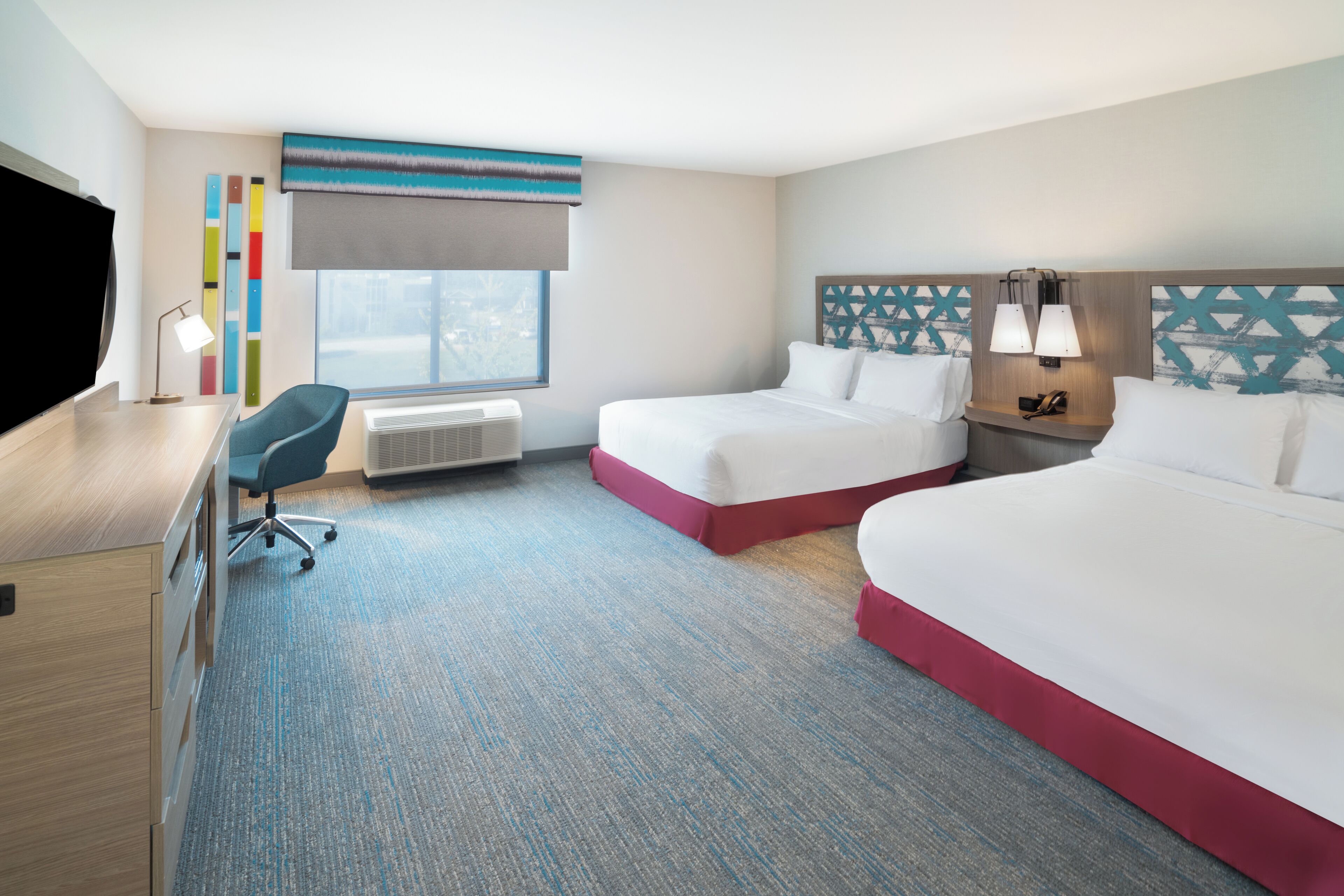 A hotel room with two beds, a desk, a chair, a TV, and a window with a view.