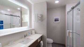 A modern bathroom with a large mirror, a sink, a toilet, and a glass-enclosed shower.