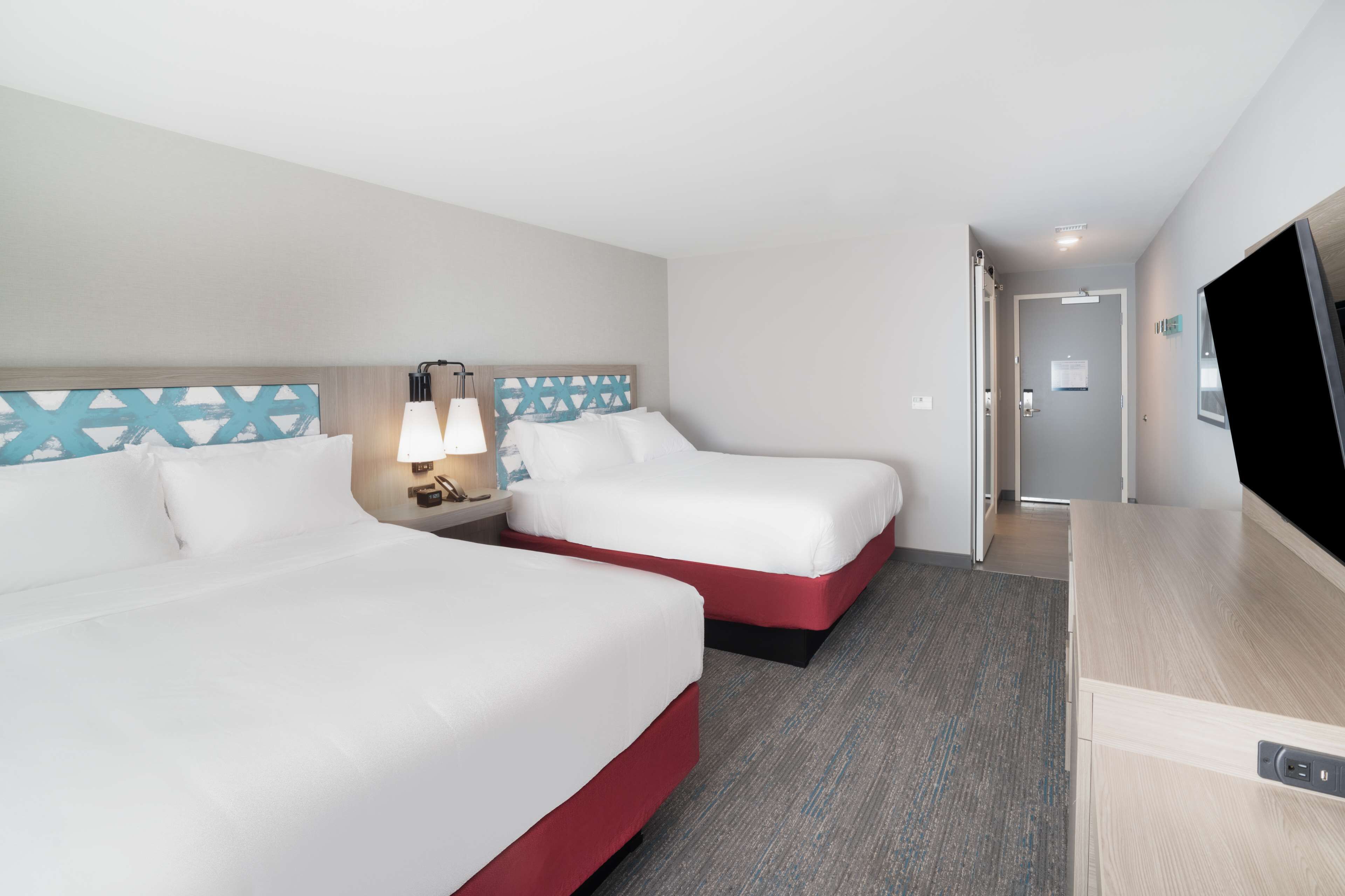 A hotel room with two beds, a TV, a desk, and a lamp.