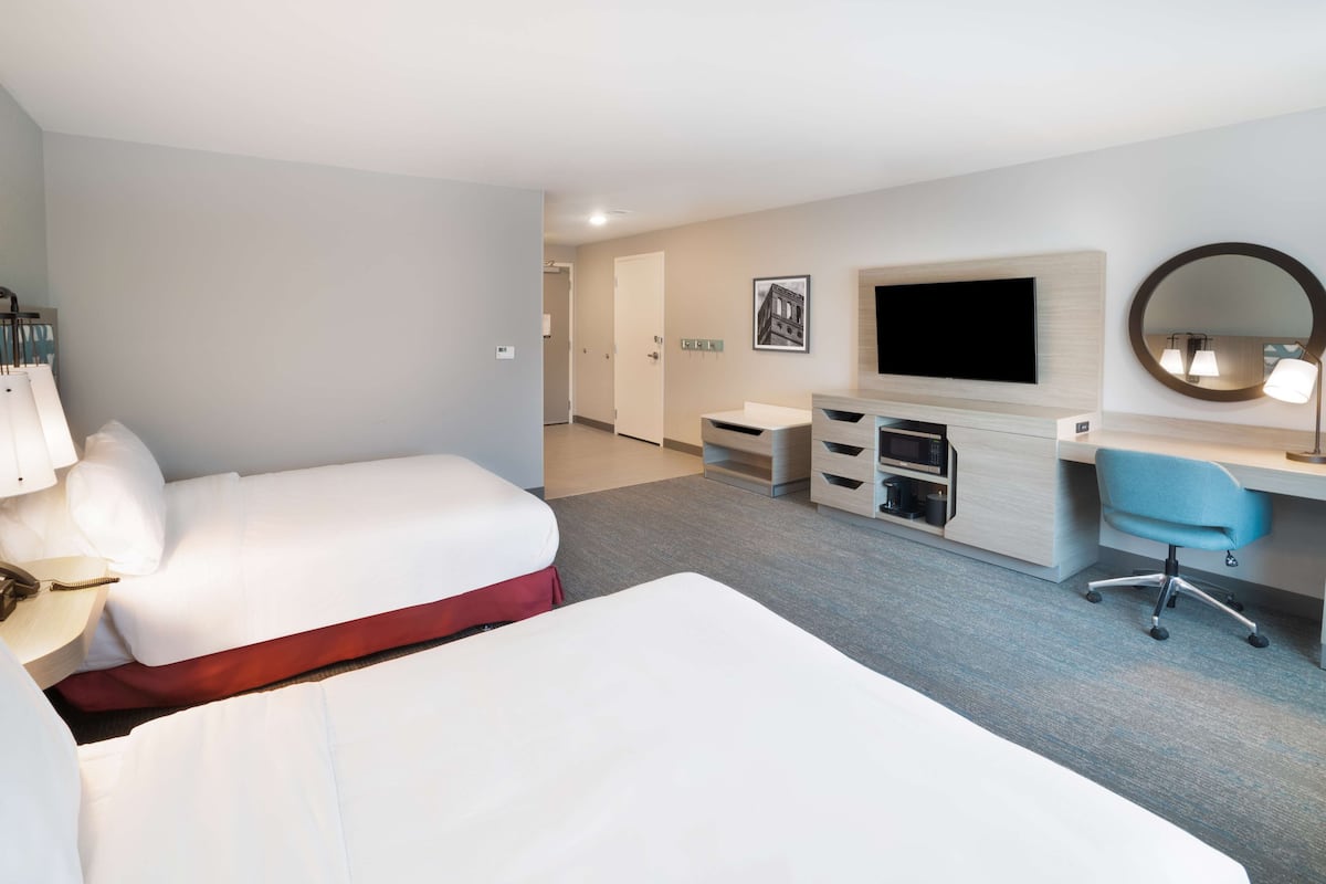 Habitación de hotel con dos camas, un escritorio, una silla, un televisor y un espejo.