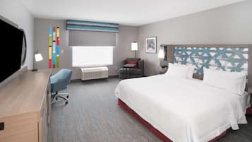 A hotel room with a large bed, a desk, a chair, a TV, and a window with blinds.