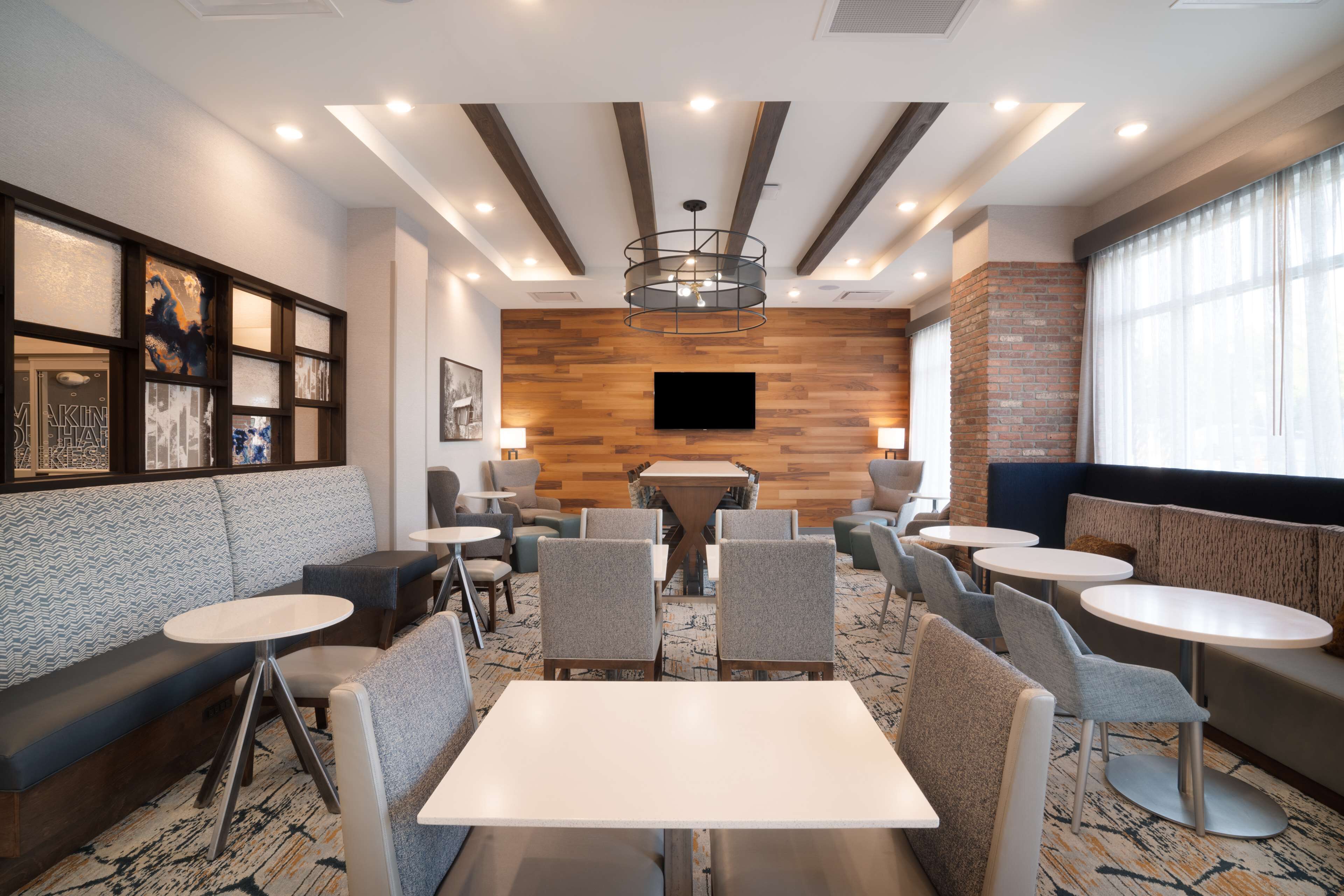 A modern hotel lobby with seating areas, a central table, and a mounted TV.