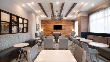 A modern hotel lobby with seating areas, a central table, and a mounted TV.
