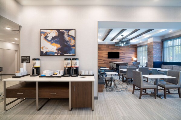 A modern hotel lobby with a breakfast bar, seating area, and a large abstract painting on the wall.