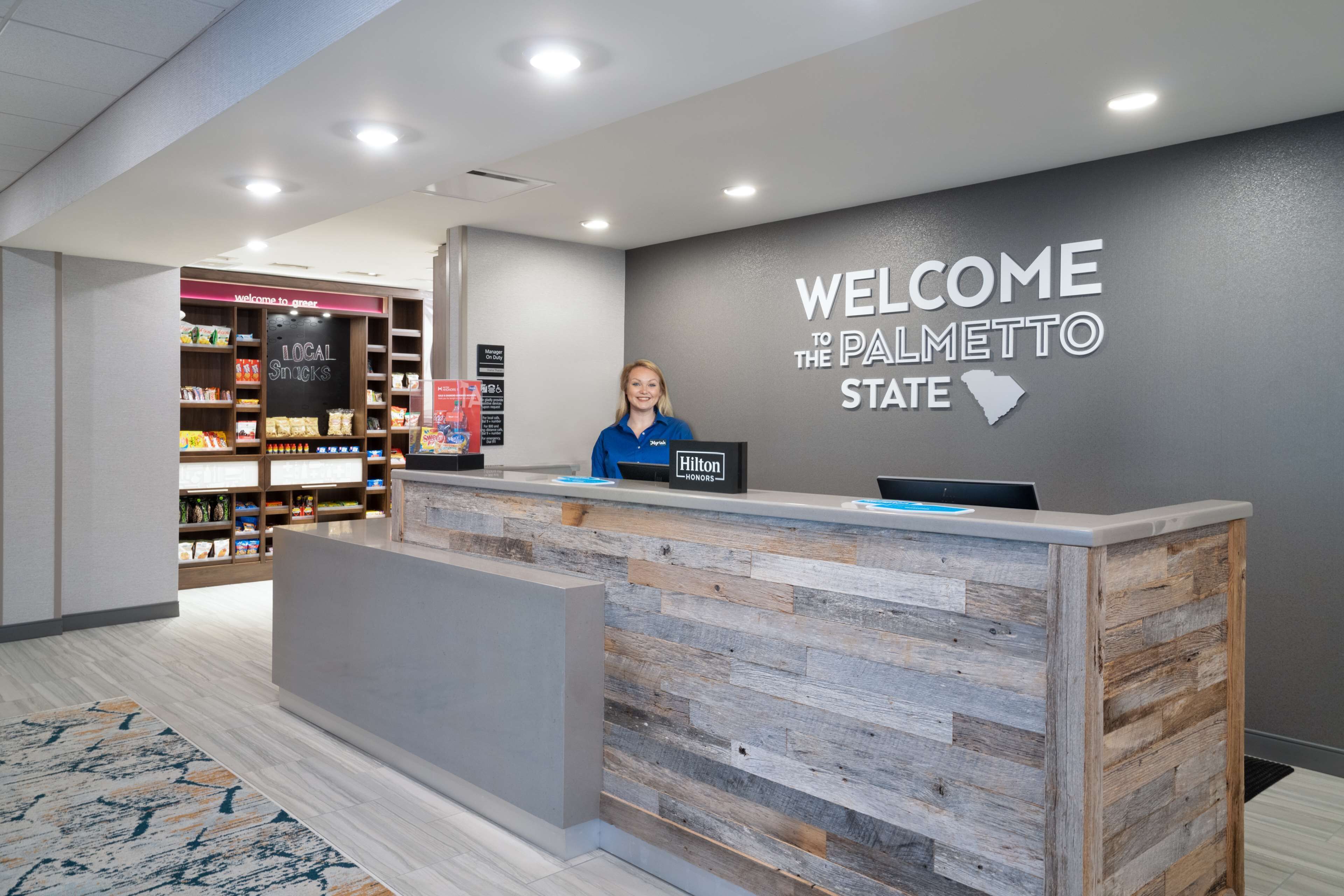 Un comptoir d’accueil orné d’une pancarte « Bienvenue dans l’État de Palmetto », d’une plaque « Hilton Honors » et d’une étagère proposant des « en-cas locaux ».