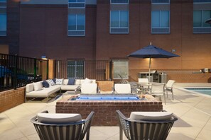 A patio with a brick fire pit, outdoor seating, and a pool.