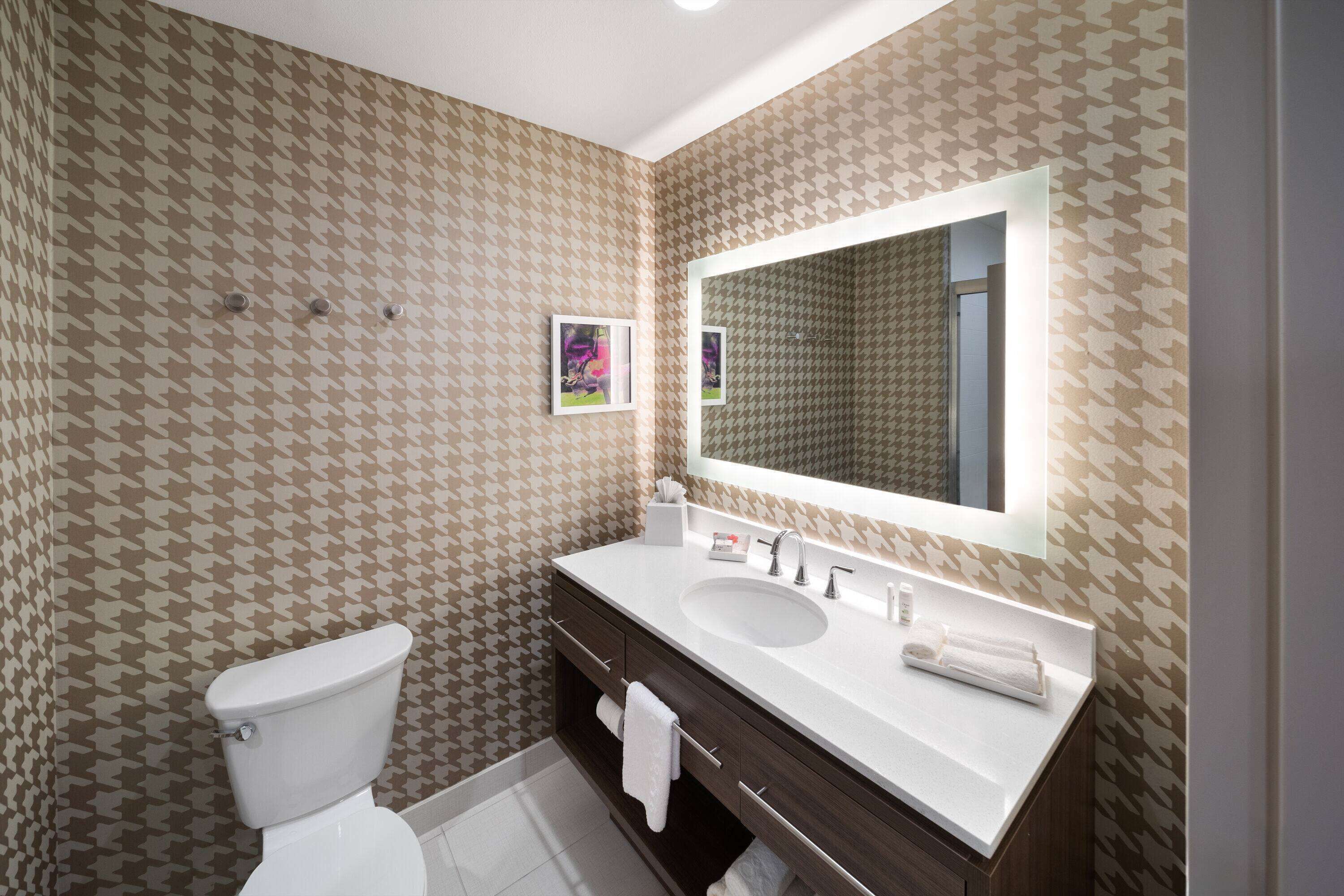 Un baño con papel tapiz estampado, un inodoro blanco, un lavabo con espejo y un perchero para toallas.