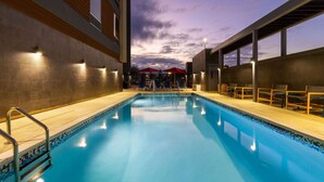 Una piscina interior con vistas al cielo, sillas junto a la piscina y una zona cubierta con sombrillas.