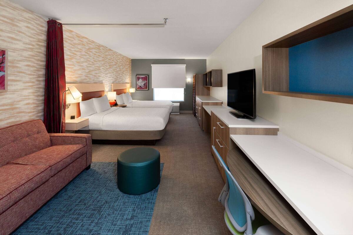 A hotel room with a sofa, two beds, a TV, and a desk.