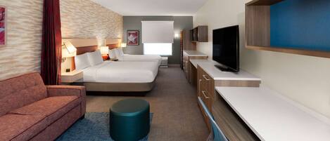 A hotel room with a sofa, two beds, a TV, and a desk.