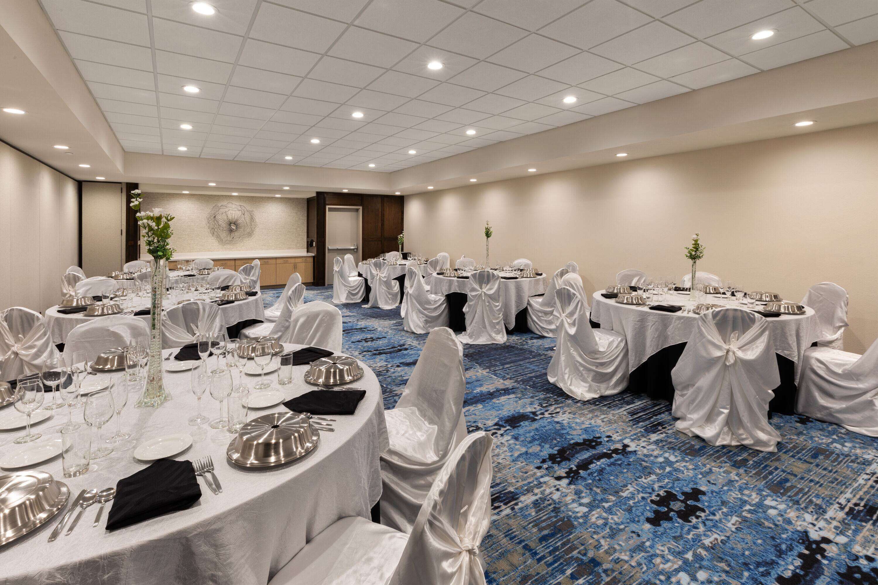 A conference room with round tables, white tablecloths, and chairs covered in white fabric.