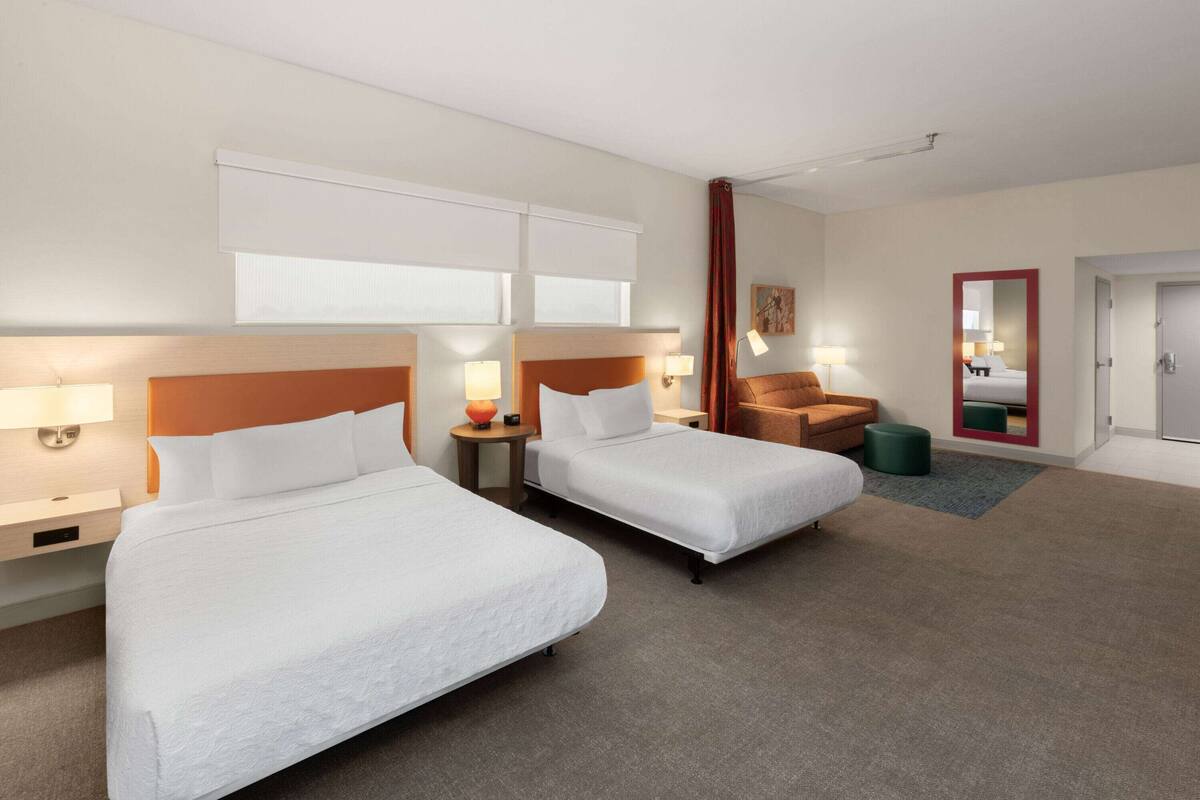 A hotel room with two beds, a chair, a small table, and a mirror.