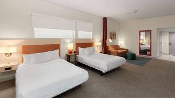 Habitación de hotel con dos camas, una silla, una mesita y un espejo.