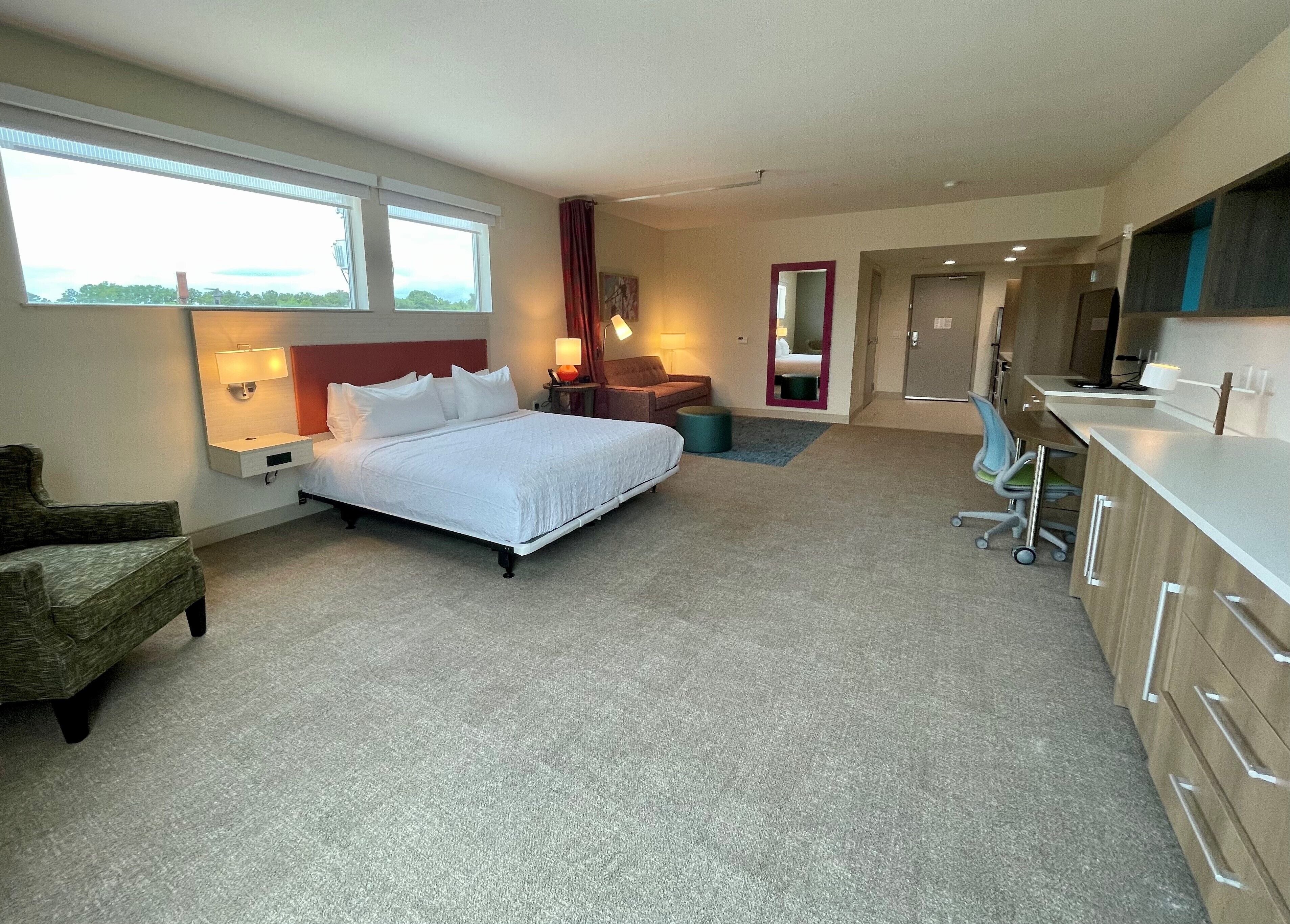 A hotel room with a bed, a desk, a chair, a bathroom, and a view of the outdoors.