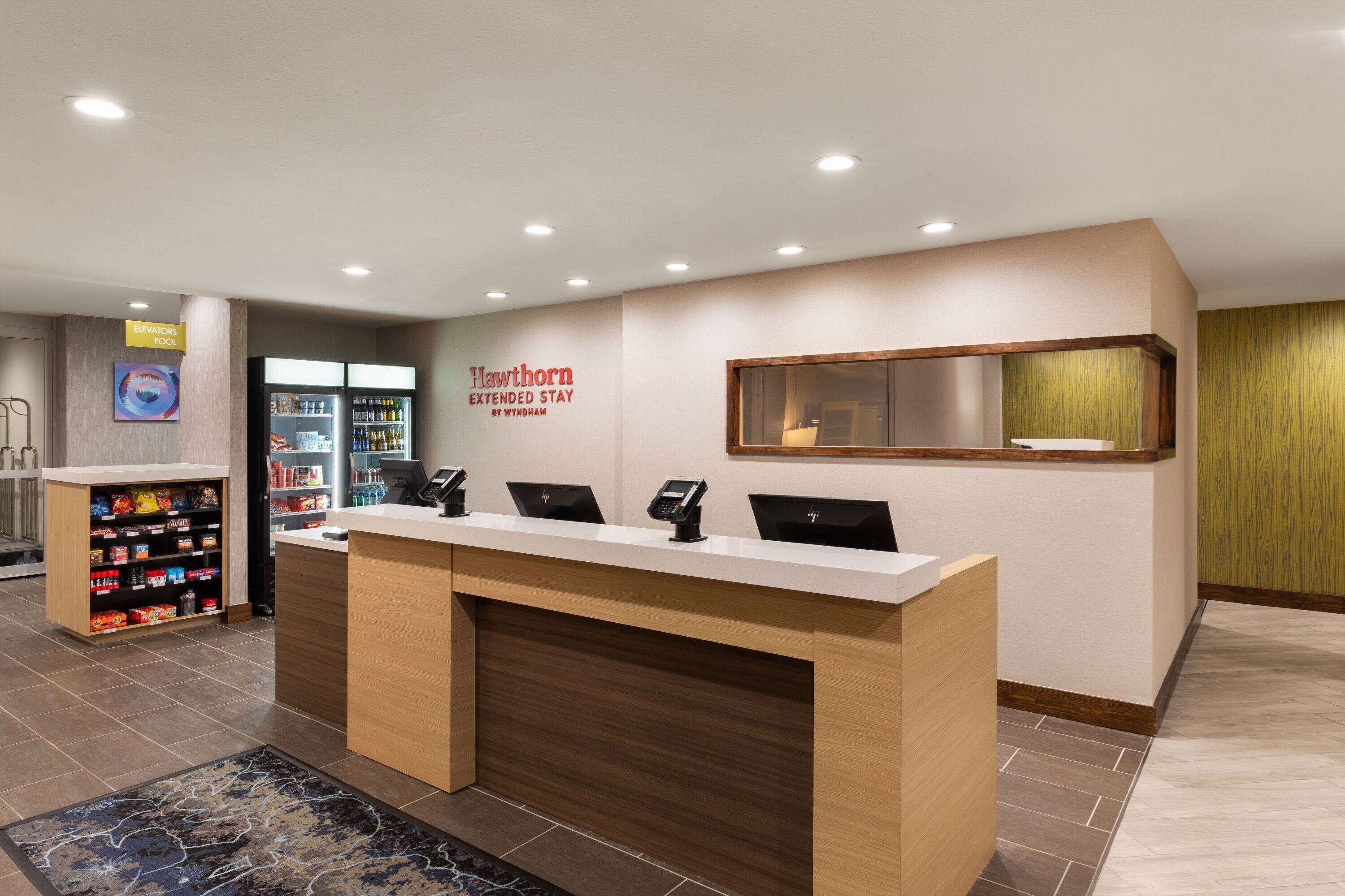 A hotel reception area with a reception desk, a sign for the Hawthorn Extended Stay by Wyndham, and a vending machine.