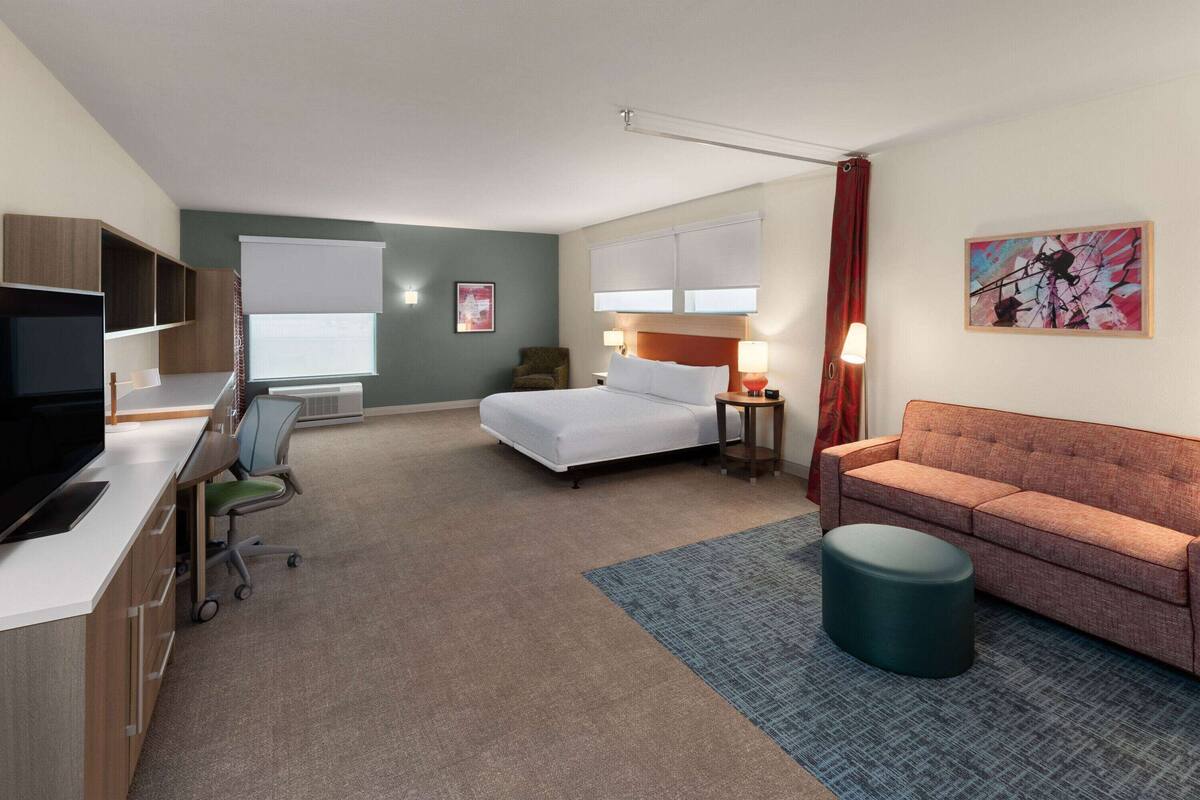 A hotel room with a bed, a sofa, a desk with a computer, a chair, and a TV.