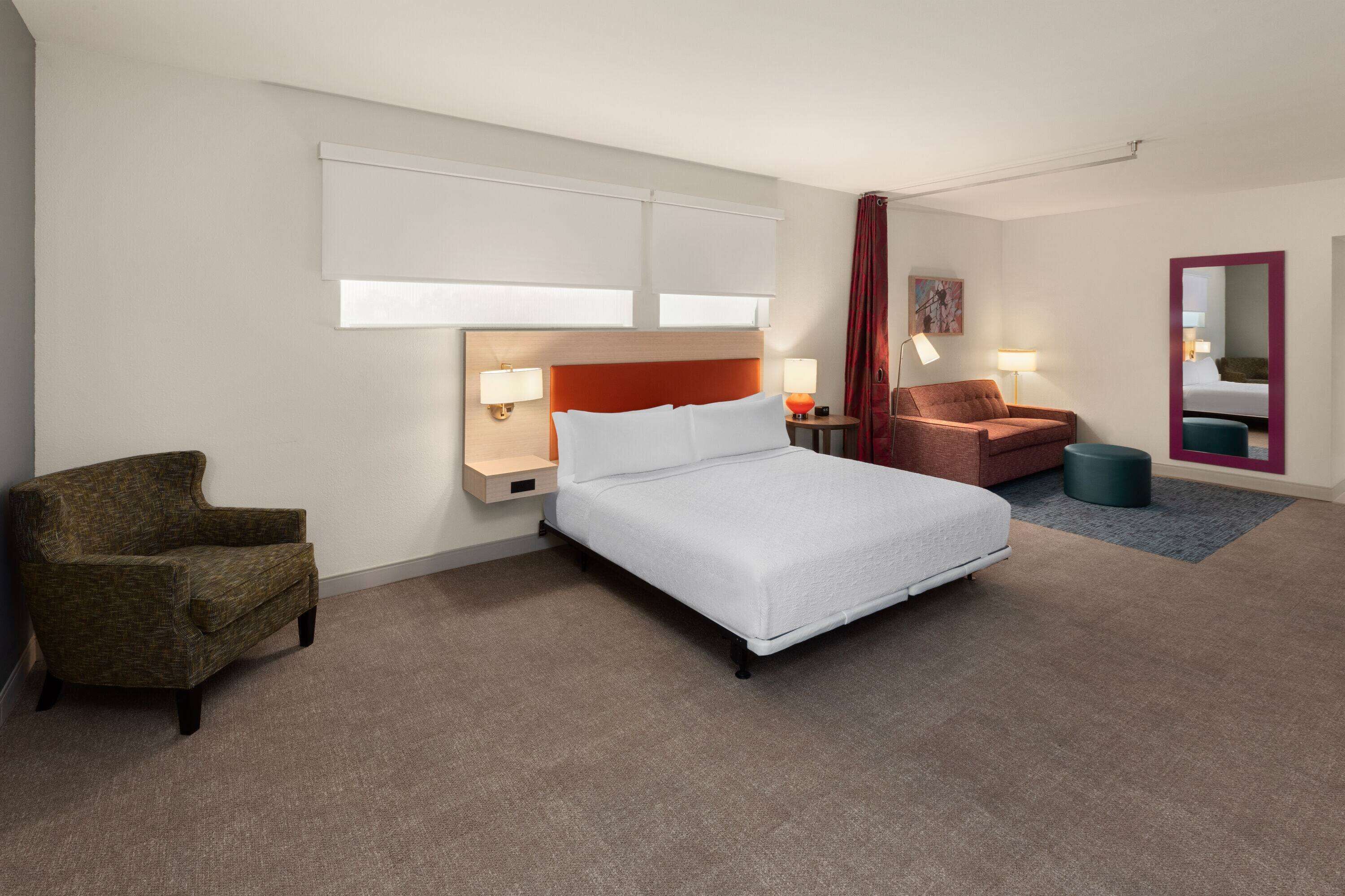 Une chambre d’hôtel moderne avec un grand lit, un canapé, un fauteuil et une petite table ronde.