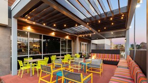 Un patio al aire libre con sillas amarillas, un sofá largo y una zona de bar con botellas.