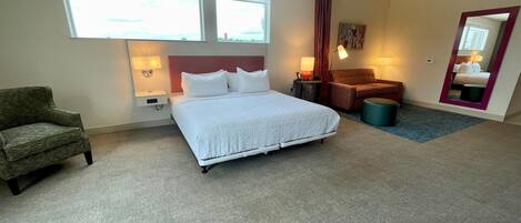 Ein Hotelzimmer mit einem großen Bett, einem Sessel, einem Schreibtisch und einem Spiegel.