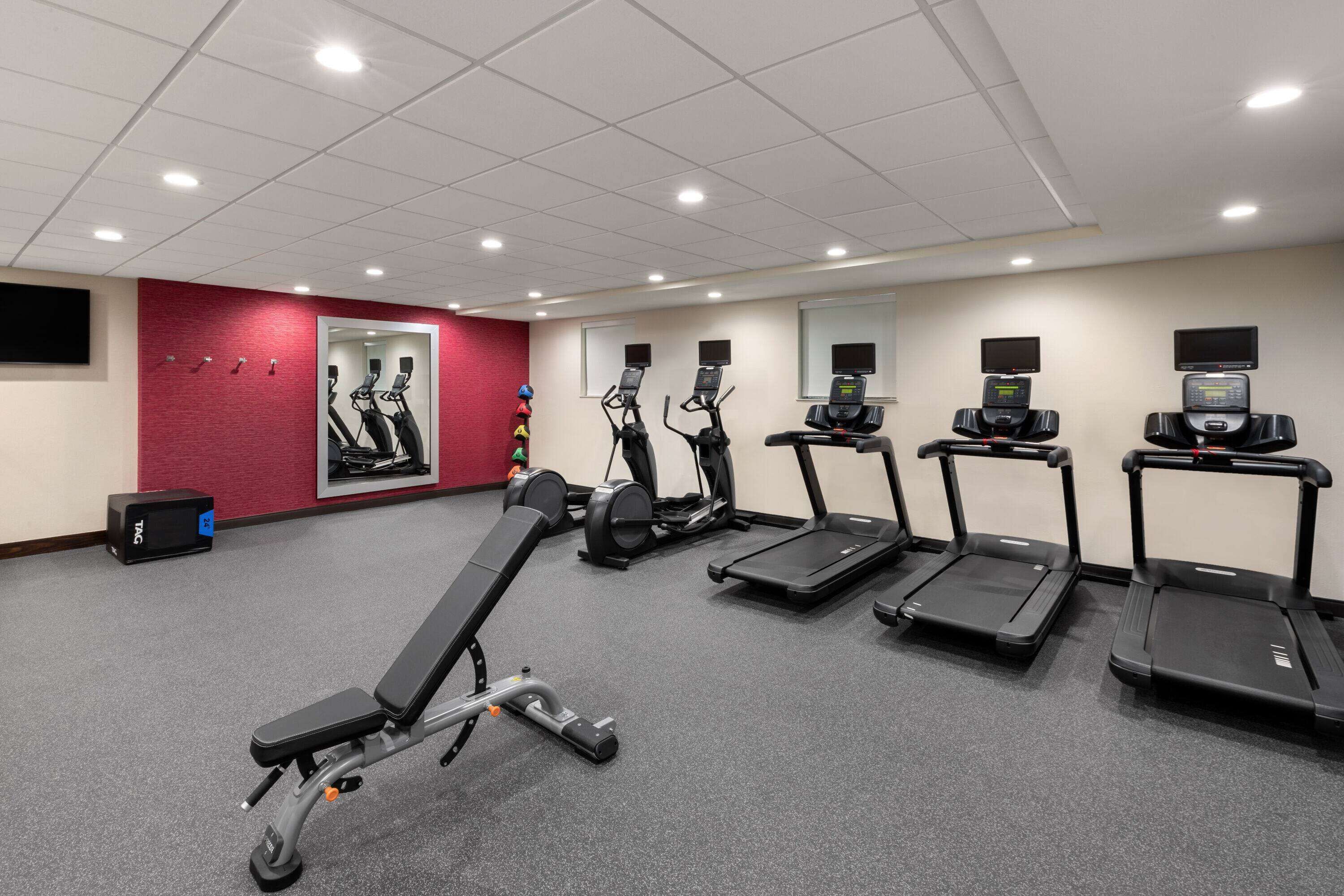 A gym with treadmills, elliptical machines, and a bench.