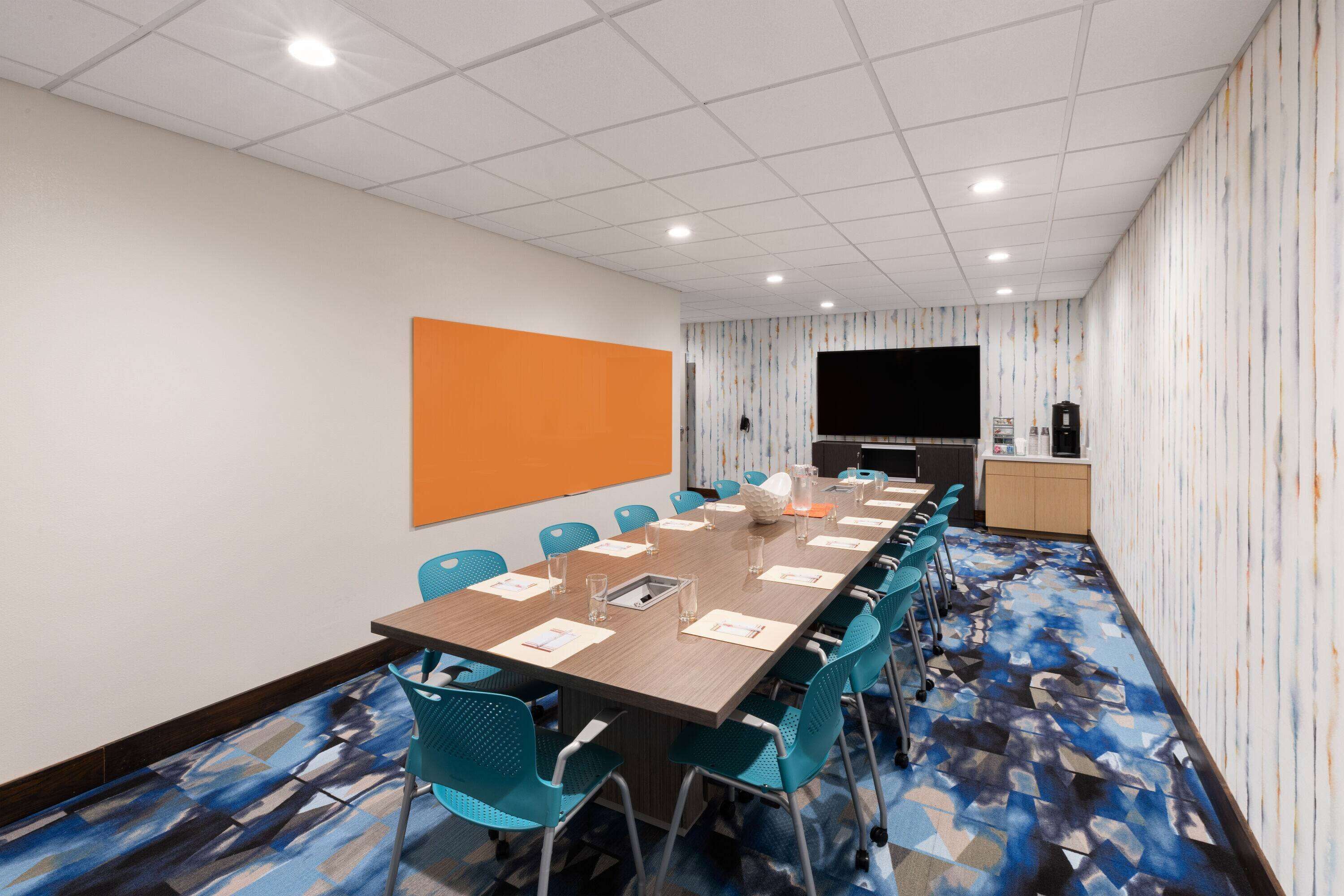 A conference room with a long table, blue chairs, a large screen, and a patterned carpet.